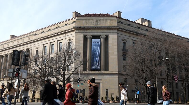 FILE - Tourists walk past a banner with President Donald Trump hanging on the Department of Justice, Feb. 27, 2026, in Washington. (AP Photo/Rahmat Gul, File)