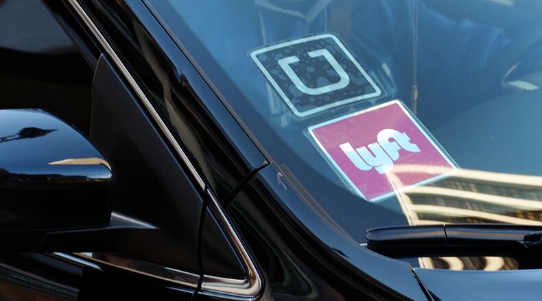 FILE - In this Tuesday, Jan. 12, 2016, file photo, a driver displaying Lyft and Uber stickers on his front windshield drops off a customer in downtown Los Angeles. Hailing a ride with a smartphone app in many U.S. cities could come down to a fight over fingerprints. Following incidents where Uber drivers were found to have criminal records, a growing number of state and local governments want ride-hailing drivers to undergo fingerprint background checks. Uber and its chief rival, Lyft, have fought those checks, contending their own method of vetting drivers is just as safe. (AP Photo/Richard Vogel, File)