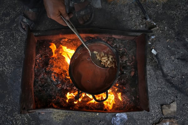 A Palestinian mother cooks beans over a fire fueled by burning plastic at a tent sheltering displaced families in Gaza City, Saturday, May 24, 2025. (AP Photo/Jehad Alshrafi)