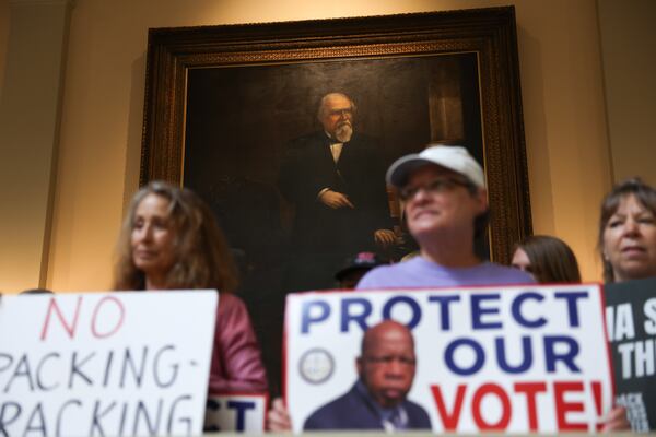 Democratic activists opposed to redistricting hold signs in front of a painting of Reconstruction-era Gov. Charles Jenkins at a news conference before the state legislature convenes for a special session in Atlanta last week. (Arvin Temkar/AJC)