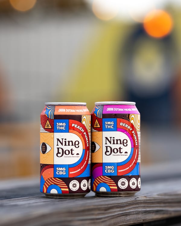 Two cans of Nine Dot beverages resting on a wooden plank.