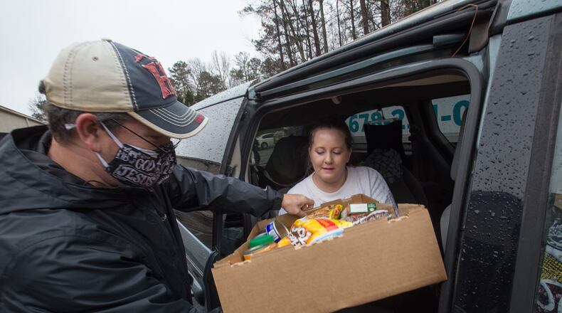A December photo of volunteering at a food bank. Mark Jeffreys, left, distributes dry goods, fresh vegetables and frozen meats to Jenny Allison, right, at New City Church in Peachtree City. Many participants regularly visit food lines and some collect for elderly and a few have never been to food banks before. This week, Johns Creek and East Point announced the cities are offering emergency financial assistance to residents experiencing hardship during the pandemic. Funds are provided to help with rent, mortgage, utilities and food. (Jenni Girtman for The Atlanta Journal-Constitution)