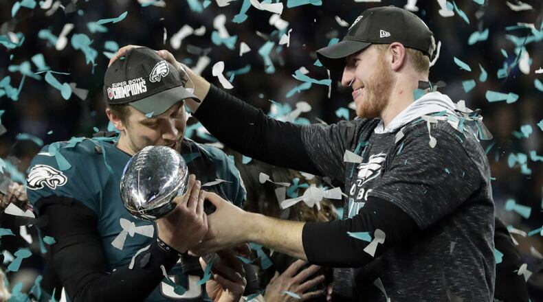 In this Feb. 4, 2018 photo, Philadelphia Eagles quarterback Carson Wentz, right, hands the Vincent Lombardi trophy to Nick Foles after winning the NFL Super Bowl 52 football game against the New England Patriots in Minneapolis. The Eagles won 41-33. President Donald Trump has called off a visit by the Philadelphia Eagles to the White House Tuesday due to the dispute over whether NFL players must stand during the playing of the national anthem.