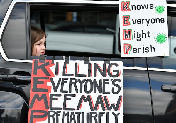 Maddie Nichols, 8, sits in the car as her mother Blythe Nichols (not pictured) decorates with signs before they participate in Drive-By protest against Gov. Brian Kemp's decision to re-open some Georgia businesses on Friday, April 24, 2020. (Hyosub Shin / Hyosub.Shin@ajc.com)
