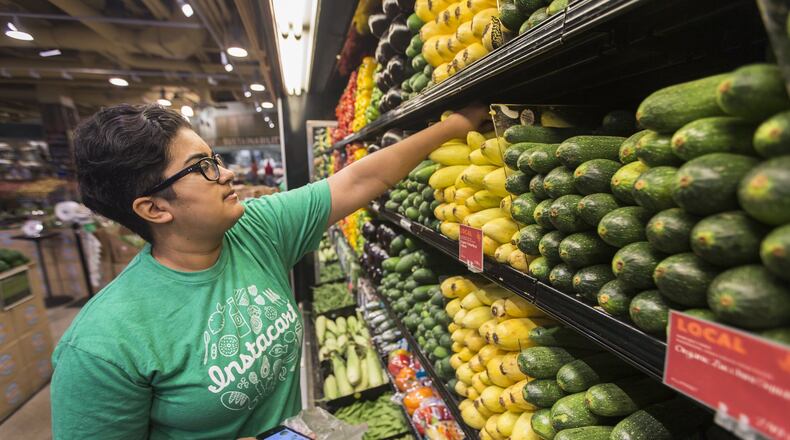 Instacart employee checks phone for list of customer orders while picking out items at a Whole Foods. (AJC file photo)