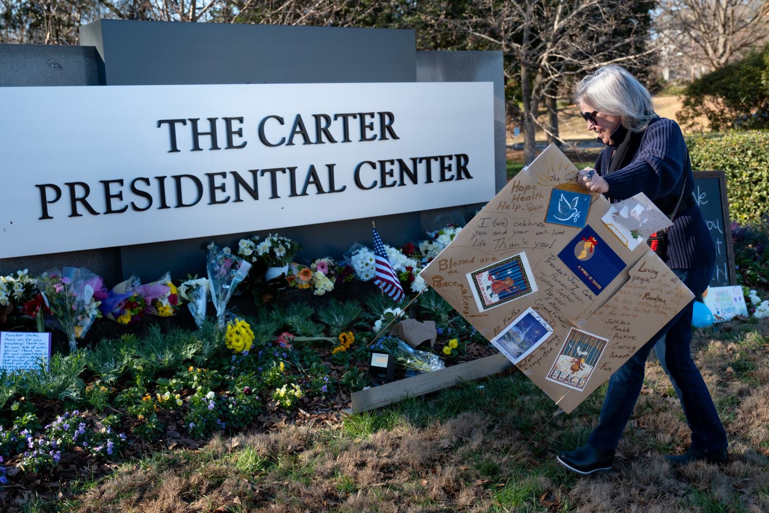 Jennifer Lund brings a handmade sign to the makeshift memorial to former President Jimmy Carter at the Carter Center in Atlanta on Monday, Dec. 30, 2024. Lund said she thinks Carter was one of the most incredible human beings.   Ben Gray for the Atlanta Journal-Constitution