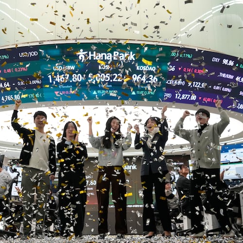 Currency traders celebrate as they work in the office with a screen showing the Korea Composite Stock Price Index (KOSPI), center top, of over 5,000 points at the foreign exchange dealing room of the Hana Bank headquarters in Seoul, South Korea, Thursday, Jan. 22, 2026. (AP Photo/Ahn Young-joon)