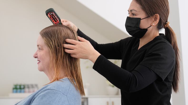 Head spa specialist Ha Truong, right, uses a Red and Blue light brush on Liz Evans to help with hair growth and reduce bacteria while massaging the scalp to help the scalp serum absorb during a treatment at Sunday Headspa Thursday, April 16, 2026, in San Francisco. (AP Photo/Jeff Chiu)