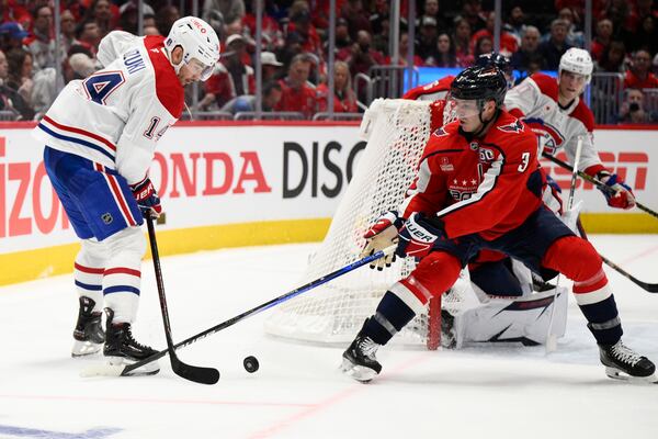 Montreal Canadiens center Nick Suzuki (14) and Washington Capitals defenseman Matt Roy (3) battle for the puck in the second period of Game 1 of a first-round NHL hockey playoff series Monday, April 21, 2025, in Washington. (AP Photo/Nick Wass)