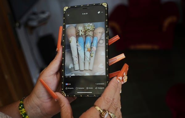 Miralys Maura Cruz, wearing long, decorative nails, shows a photo of nail designs she likes, at her home in La Gallega, Havana province, Cuba, Saturday, June 28, 2025. (AP Photo/Ramon Espinosa)