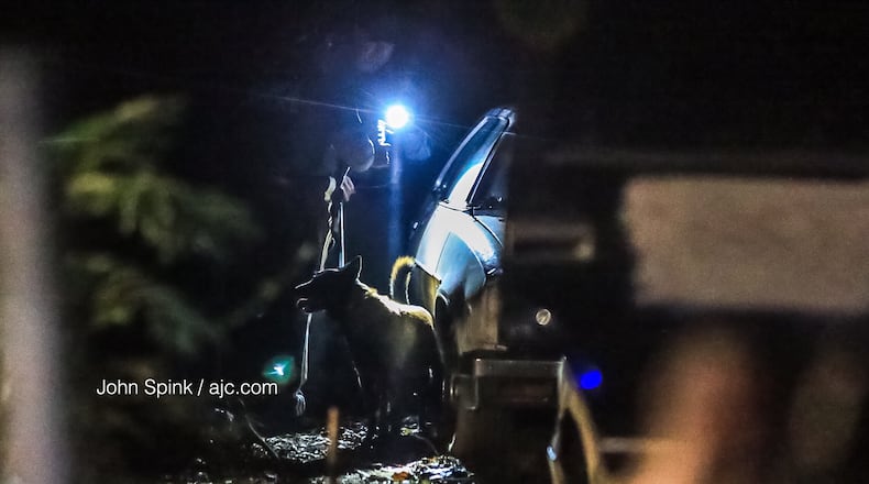 An Atlanta police K-9 officer searches a car in southwest Atlanta Tuesday morning during a manhunt for a shooter who fired at officers in an unmarked patrol car.  The shooting was one of several Atlanta police were investigating overnight.
