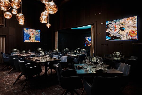 A dark restaurant interior with vivid, modern paintings on the wall and a large, modern glass chandelier.