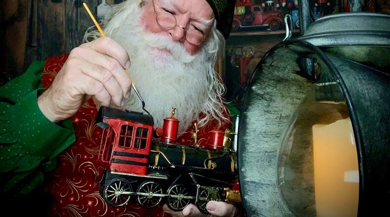 Derek "Santa Derek" Dugan working on a train in front of his virtual workshop background, which he is using to do virtual visits with children this year due to the coronavirus. Courtesy of Dugan