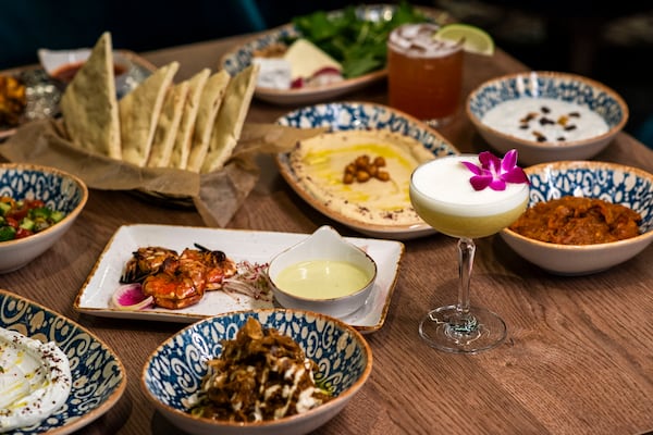 A table full of Persian dishes, including a cocktail with an edible flower, pita, dips and mezze