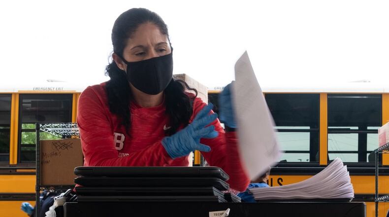 Berkmar High School assistant principal Gypsy Hernandez picks up paperwork and a computer to give to a student who came to the school April 7. Although administrators have been back working at schools for weeks, a summons for teachers and other staff to return to on-site learning met with public outcry. Ben@BenGray.com for the Atlanta Journal-Constitution