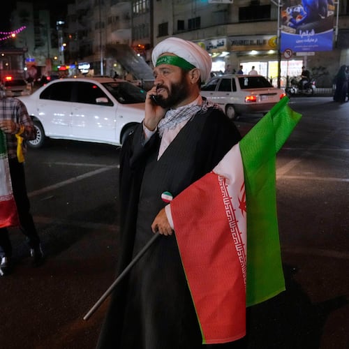 A cleric speaks on his cellphone holding an Iranian flags for a pro-government campaign in downtown Tehran, Iran, Friday, May 8, 2026. (AP Photo/Vahid Salemi)