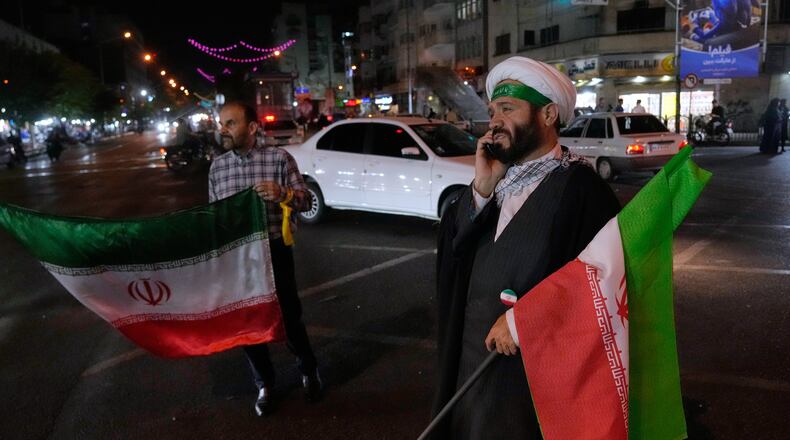 A cleric speaks on his cellphone holding an Iranian flags for a pro-government campaign in downtown Tehran, Iran, Friday, May 8, 2026. (AP Photo/Vahid Salemi)