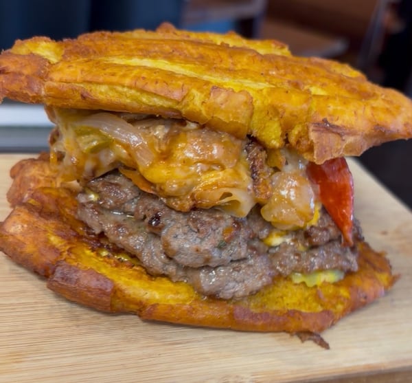 Two burger patties topped with cheese and sauteed onions are in between two fried plantains (instead of a bread bun).