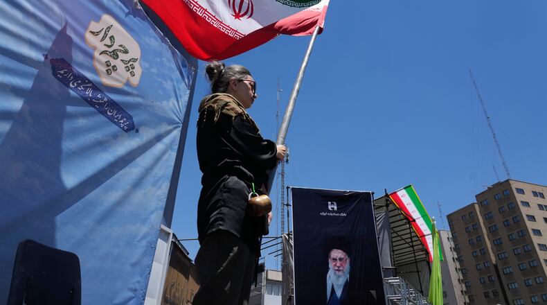 A woman waves an Iranian flag during a pro-government campaign as a portrait of the slain Supreme Leader Ayatollah Ali Khamenei, who was killed in U.S. and Israeli strikes on Feb. 28, is displayed at right, in downtown Tehran, Iran, Monday, June 15, 2026. (AP Photo/Vahid Salemi)