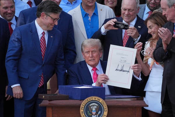 President Donald Trump holds his signed signature bill of tax breaks and spending cuts at the White House, Friday, July 4, 2025, in Washington, as House Speaker Mike Johnson of La., left, watches and Rep. Steve Scalise, R-La., takes a photo. (AP Photo/Evan Vucci)