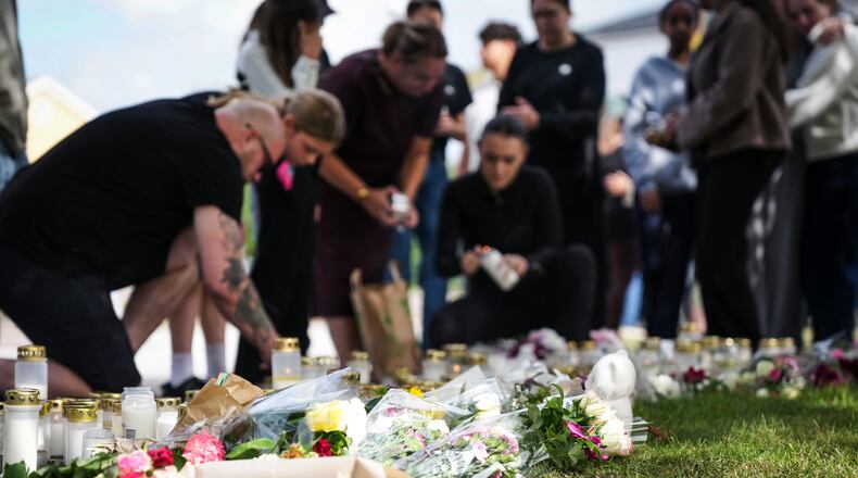 People leave flowers and candles at a makeshift memorial outside a school in Fagersta, Sweden, Saturday Aug. 22, 2026, the day after an 18-year-old with a sword attacked the school killing one person and seriously injuring two others. (Magnus Lejhall/TT via AP)