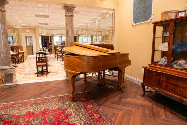 A tea room with a herringbone wood floor and a baby grand piano near the entrance in a natural wood tone.