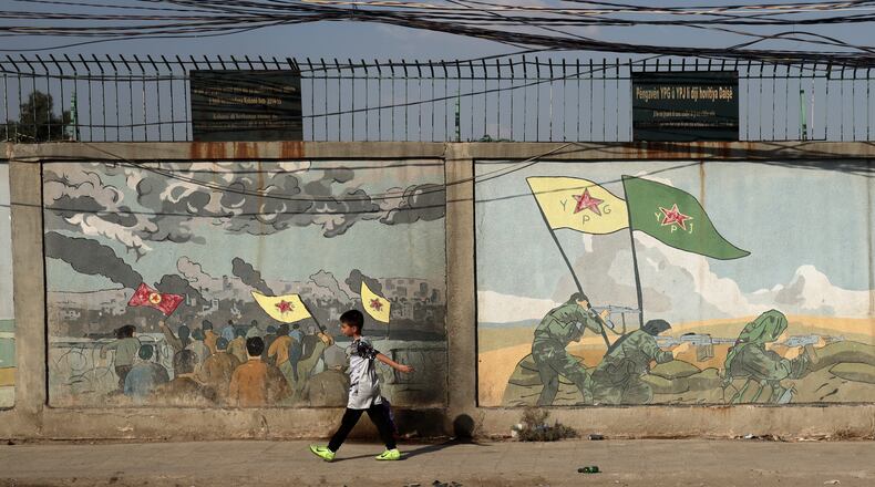 A boy walks past murals depicting Kurdish YPG and YPJ fighters battling Islamic State militants in Qamishli, northeastern Syria, Wednesday, Aug. 26, 2026. (AP Photo/Baderkhan Ahmad)