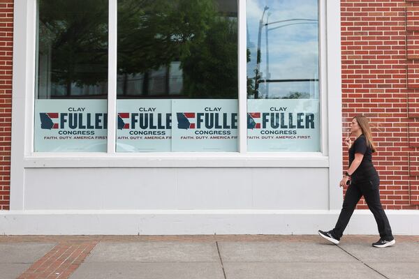 A pedestrian in Rome walks by signs endorsing Republican Clay Fuller for Congress on March 31, 2026. (Arvin Temkar/AJC)