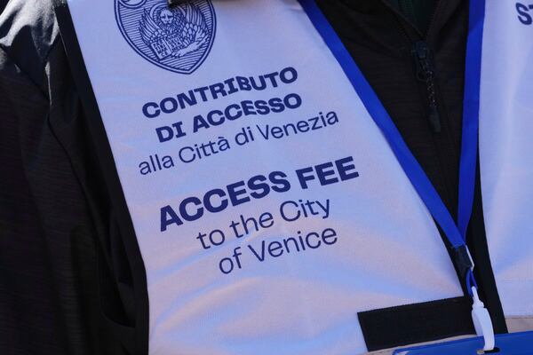 A steward's gilet states an arrival tax fee for tourists visiting Venice, Italy, Friday, April 18, 2025. (AP Photo/Antonio Calanni)