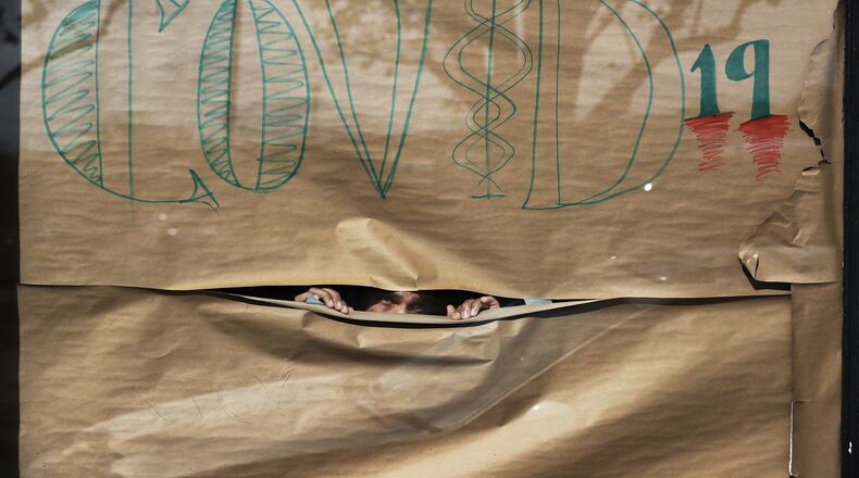 Frank Battle, of The Shop on Main Street, papers the windows of his barbershop to inform his customers he is closed for COVID-19 on Thursday, March 26, 2020, in College Park. A patchwork of local officials this week ordered the closure of businesses across the state and forced people to shutter inside their homes over fears of COVID-19. (Curtis Compton ccompton@ajc.com)