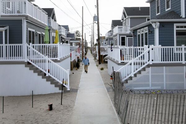 In this Oct. 15, 2014 photo, a man walks on a sidewalk in the Breezy Point neighborhood in the Queens borough of New York. Two years ago a fire raged across this oceanfront community during Superstorm Sandy, destroying 130 homes, including those that lined this walk. The new houses are all built on elevated concrete foundations to protect them from future storms. (AP Photo/Mark Lennihan)