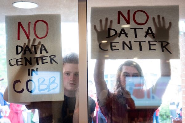 Data center opponents hold signs against a window to the Marietta City Council chambers during a meeting with an overflow crowd on Wednesday, June 10, 2026. (Ben Gray for the AJC)