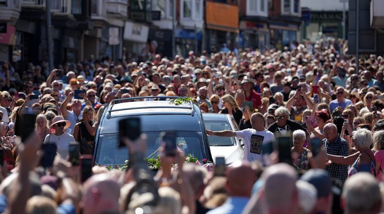 Fans of singer Bonnie Tyler line the streets as her coffin is transported in a hearse back to her former home ahead of her funeral, in Mumbles, Wales, Saturday, Aug. 15, 2026. The Total Eclipse Of The Heart musician, whose real name was Gaynor Hopkins, died in hospital in Portugal on July 8 at the age of 75. (AP Photo/Alastair Grant)