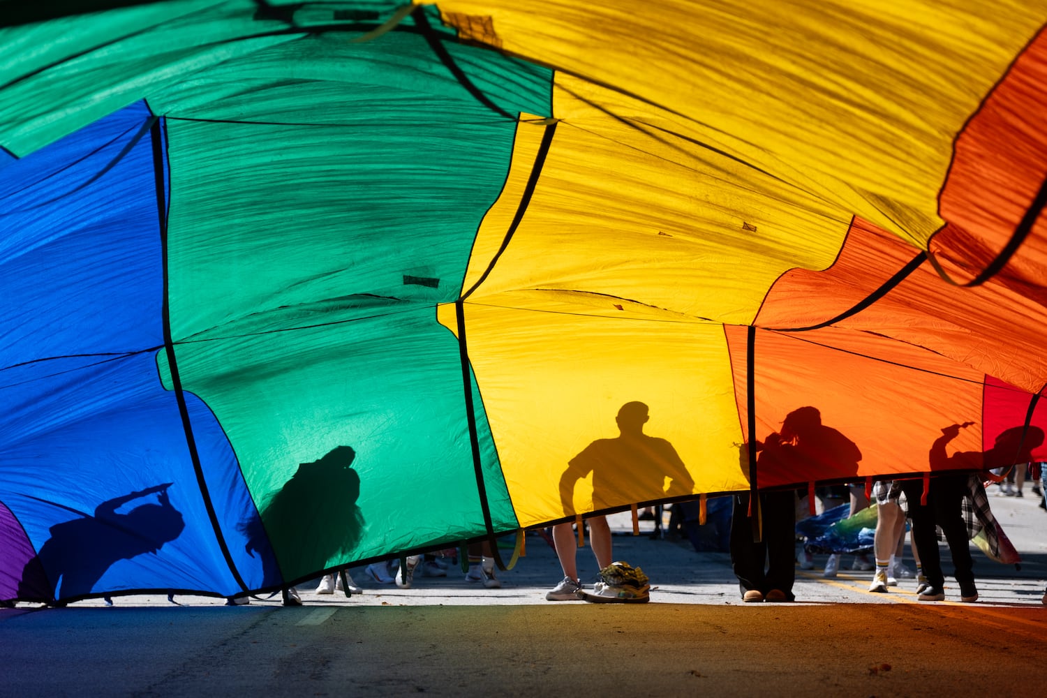 People are silhouetted against a huge Pride flag before the start of the Atlanta Pride Parade on Sunday, Oct. 12, 2025. (Ben Gray for the AJC)