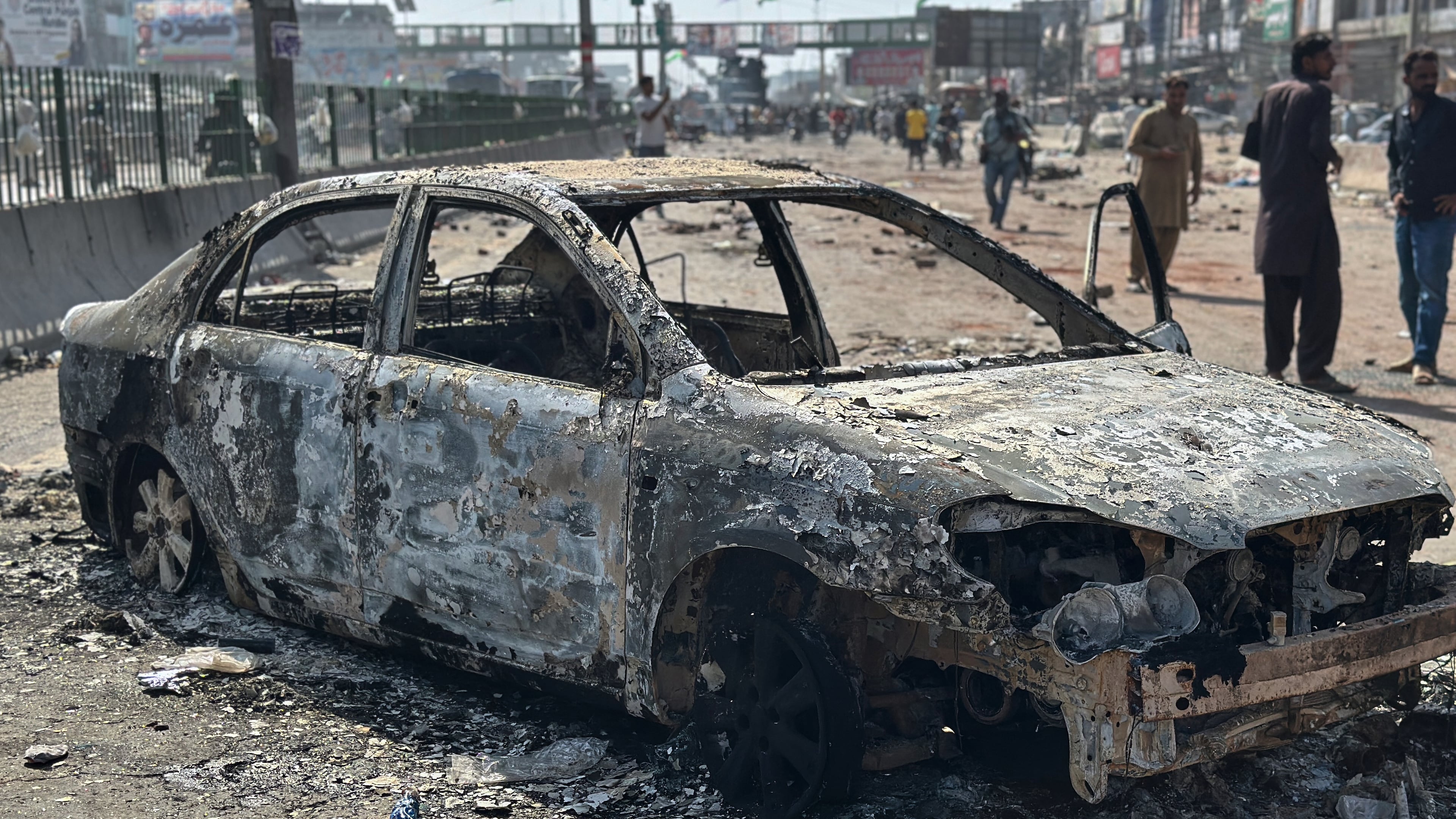 Local residents stand by burnt vehicles after police in Pakistan clashed with thousands of protesters during a march in support of Palestinians, in Muridke near Lahore, Pakistan, Monday, Oct. 13, 2025. (AP Photo/Jahanzeb Khan)