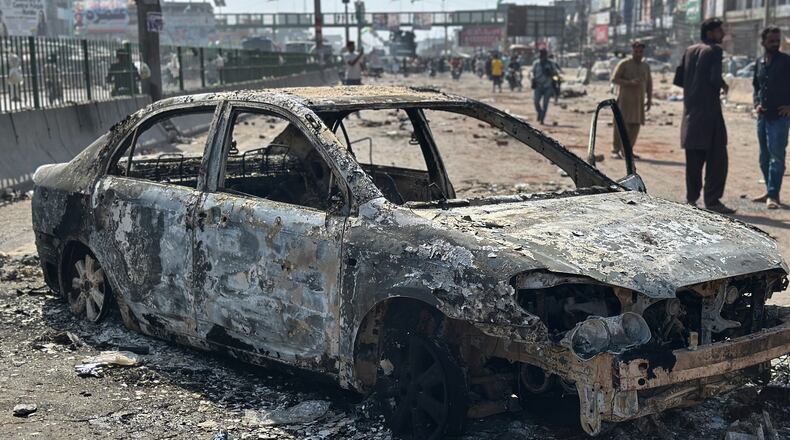 Local residents stand by burnt vehicles after police in Pakistan clashed with thousands of protesters during a march in support of Palestinians, in Muridke near Lahore, Pakistan, Monday, Oct. 13, 2025. (AP Photo/Jahanzeb Khan)