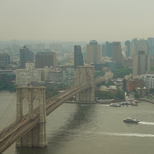 Boats maneuver the East River near the Brooklyn Bridge as smoke from wildfires blankets the sky Thursday, July 16, 2026, in New York. (AP Photo/Alyssa Goodman)