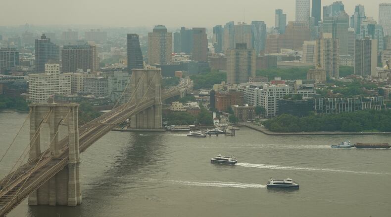 Boats maneuver the East River near the Brooklyn Bridge as smoke from wildfires blankets the sky Thursday, July 16, 2026, in New York. (AP Photo/Alyssa Goodman)