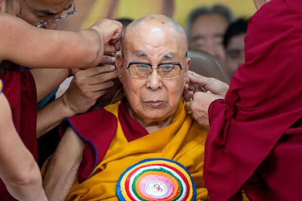 Attendant monks help put a microphone around Tibetan spiritual leader the Dalai Lama's head during his 90th birthday celebrations at the Tsuglakhang temple in Dharamshala, India, Sunday, July 6, 2025.(AP Photo/Ashwini Bhatia)