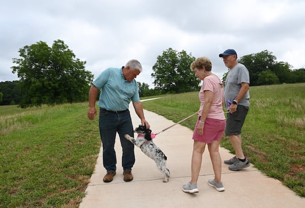 Mark Thomas (left) is greeted by Kathy and Ernie Perry’s dog, Milly, at the Thomas Farm Preserve on Wednesday, June 18, 2025, in Watkinsville. Thomas grew up on a farm on the land that is now the preserve. (Hyosub Shin/AJC)