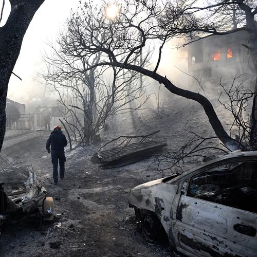 A firefighter walks through a burned area as flames engulf a house during a wildfire on the island of Salamina, west of Athens, Greece, Sunday, Aug. 16, 2026. (AP Photo/Michael Varaklas)