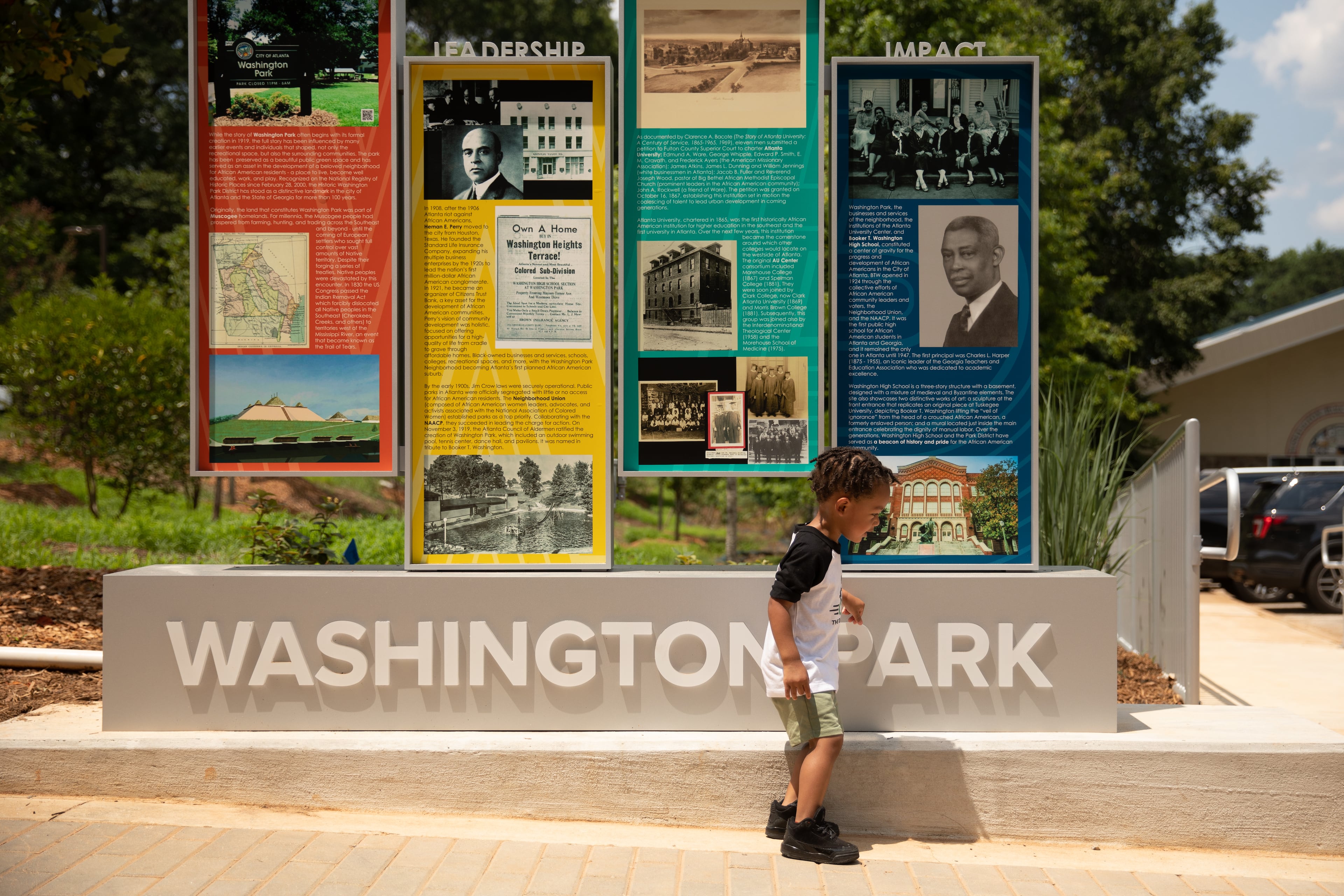 Two-year-old Epic Jones passes in front of the new Washington Park historical sign that highlights the history of Atlanta's earliest, planned Black neighborhoods on Monday, June 23, 2025. (Riley Bunch/AJC)