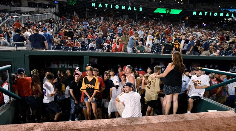 Spectators stand in the visiting team dugout during a stoppage in play due to an incident near the ballpark in the sixth inning of a baseball game between the Washington Nationals and the San Diego Padres, Saturday, July 17, 2021, in Washington. (AP Photo/Nick Wass)