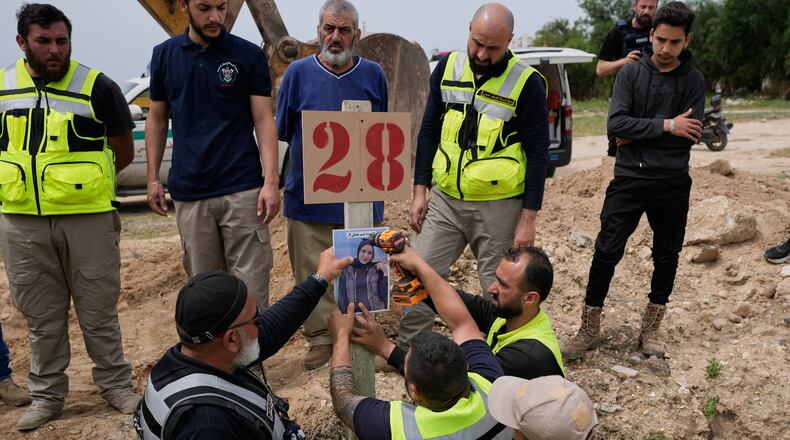 Paramedics attach a portrait over the grave of Ghadir Baalbaki, 19, who was killed on Tuesday in an Israeli airstrike, at a temporary mass grave in the southern port city of Tyre, Lebanon, Wednesday, April 15, 2026. (AP Photo/Hussein Malla)