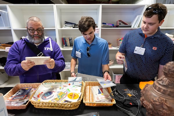 (L-R) RD Dewberry, Robert Phillips and Ryan Cook look at vintage stickers and airline timetables at the Delta Flight Museum Surplus Sale in Atlanta on Friday, Oct. 10, 2025. Every month, Delta fans wait in line for hours for the chance to buy vintage airline merch. (Arvin Temkar/AJC)