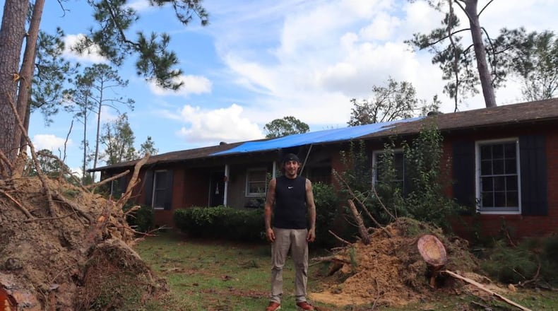 Daniel Shahan surrounded by two trees that fell during Hurricane Helene in his front yard, a week after the storm. Last year a tree struck his house where the blue tarp currently lays from Hurricane Idalia. Oct. 3, 2024. (Photo Courtesy of Kala Hunter)