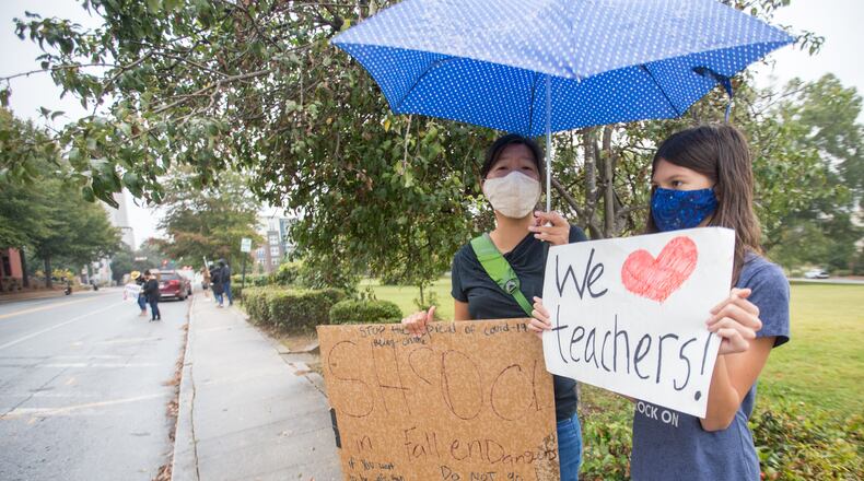 Teachers, parents and students, including Keri Chaya, left, and her daughter 10-year-old Calla Lockwood, right, protest in front of the Decatur City School Headquarters on Trinity Place in response to the district's plan to return teachers to schools in an effort to get back to in-person learning Friday, Oct, 9, 2020.  (Jenni Girtman for The Atlanta Journal-Constitution)