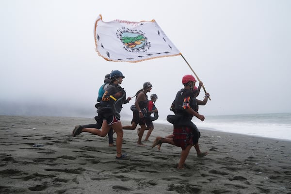 Youth from the Hoopa Valley Tribe run with a flag across a sandy stretch that separates the Klamath River from the Pacific Ocean on Friday July 11, 2025, in Klamath, Calif. (AP Photo/Brittany Peterson)