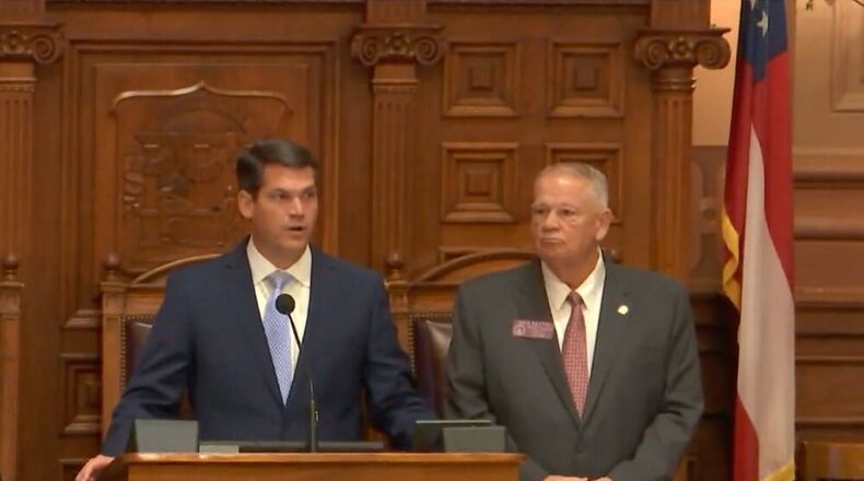 (left) white man standing at podium with navy jacket and blue tie. (right) white man with short white hair with grey jacket, red tie.