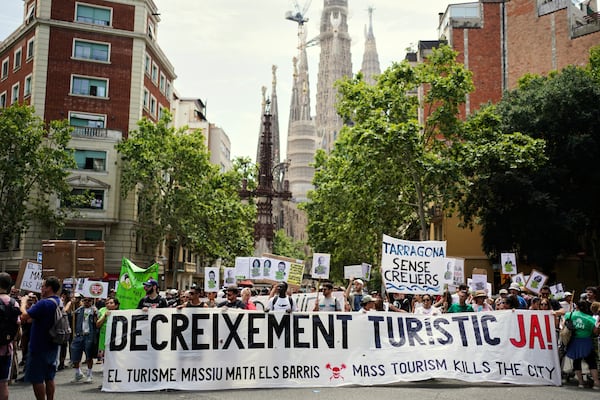 People march near the Sagrada Familia basilica during a protest against overtourism in Barcelona, Spain, Sunday, June 15, 2025. Main banners read 'Decrease level of tourism now', Mass tourism kills neighborhoods' and 'Tarragona without cruise ships' (AP Photo/Pau Venteo)